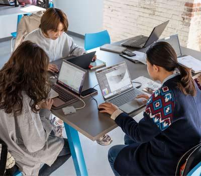 3个学生坐在桌子旁，用笔记本电脑